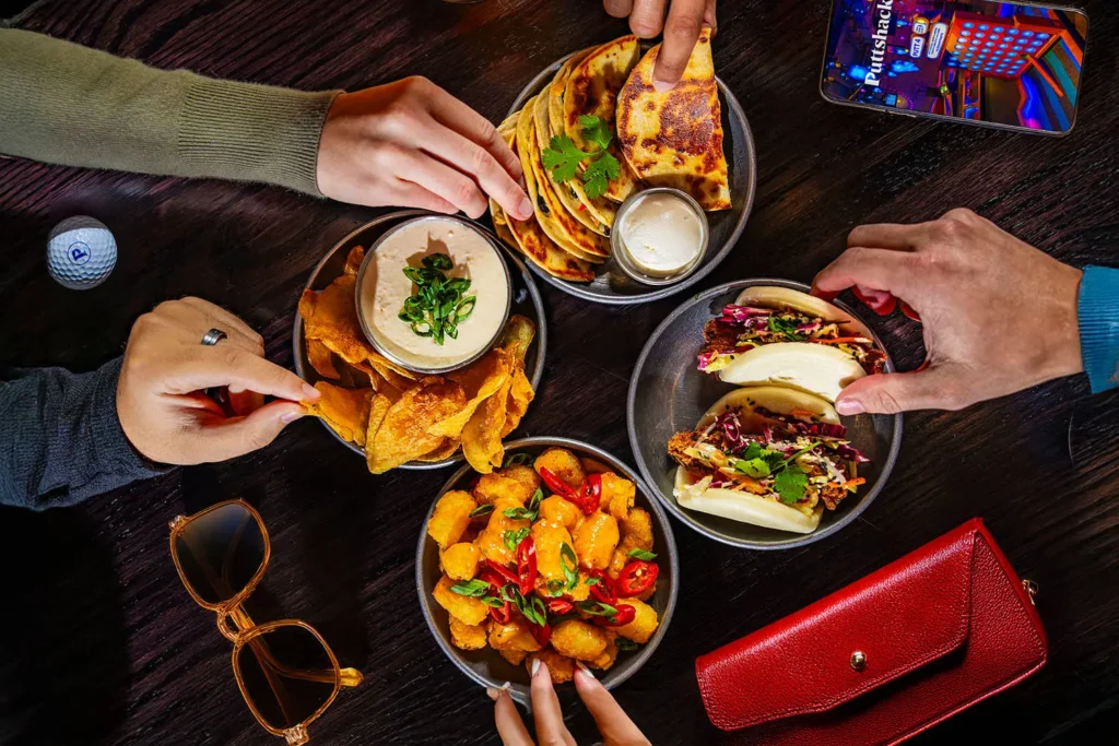 Four appetizers with people’s hands reaching out to grab them.