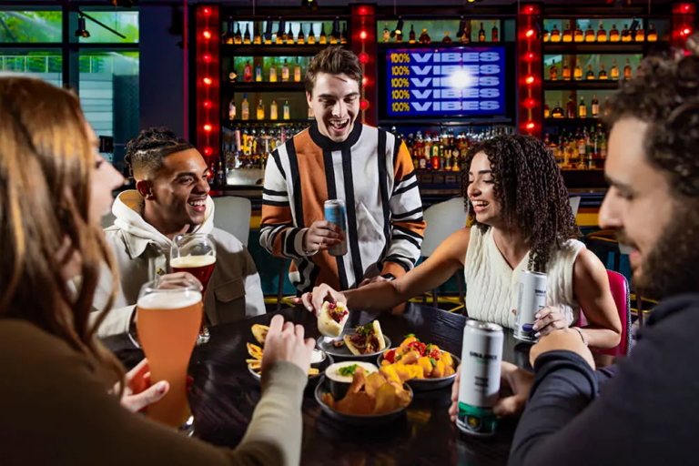 Three men and two women sharing and enjoying food and drinks at a table in Puttshack