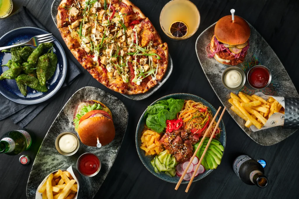 Layout of food and drinks: Peppers, flatbread, burger, asian noodles, pulled pork, and fries